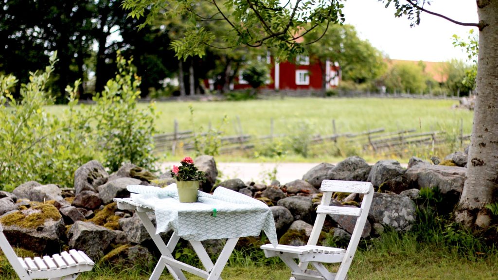 Bild på bord med stolar med stenmur och grönska bakom på Bråbo B&B.
