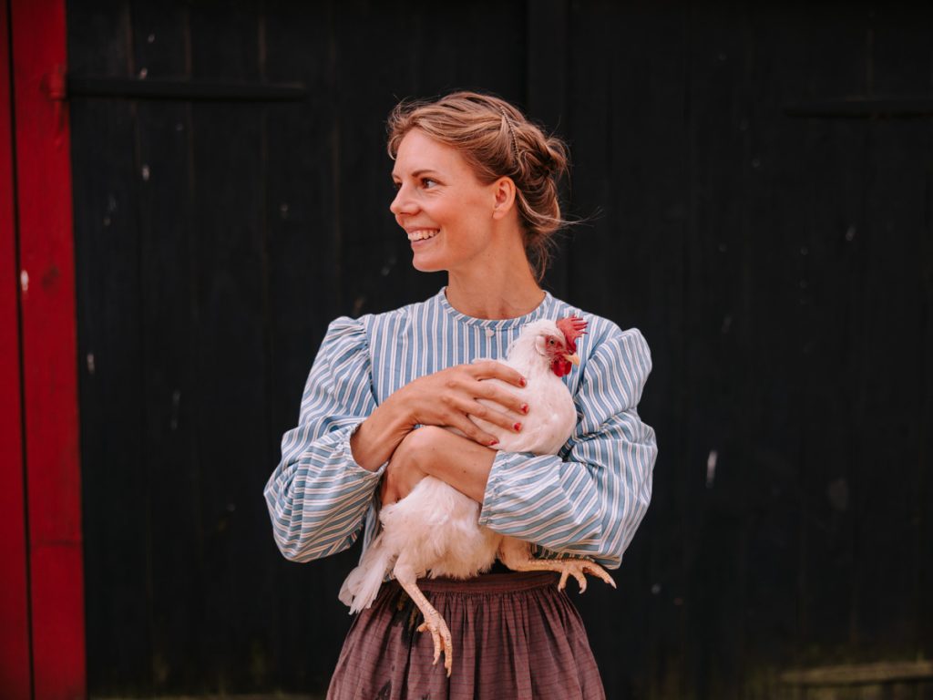 Bild på Frida Persson, trädgårdsmästare i Stensjö by, som håller i en höna.