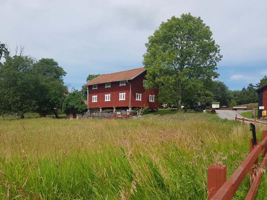 Bild på rött laduhus i Fallebo gård i Oskarshamn med en stor grön äng framför.
