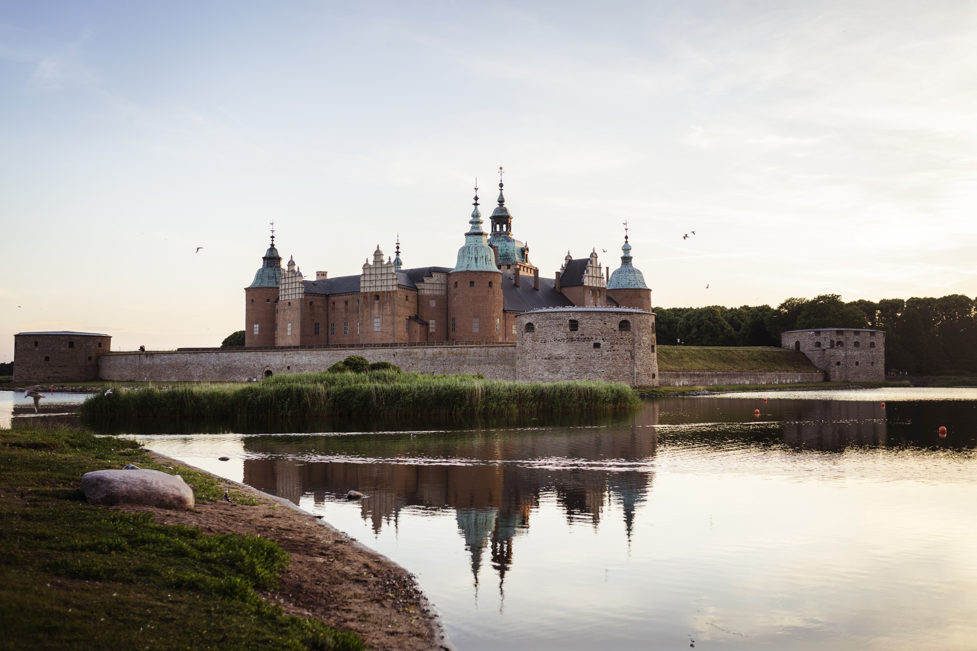 Kalmar slott, vars siluett speglas i det blanka vattnet utanför murarna.