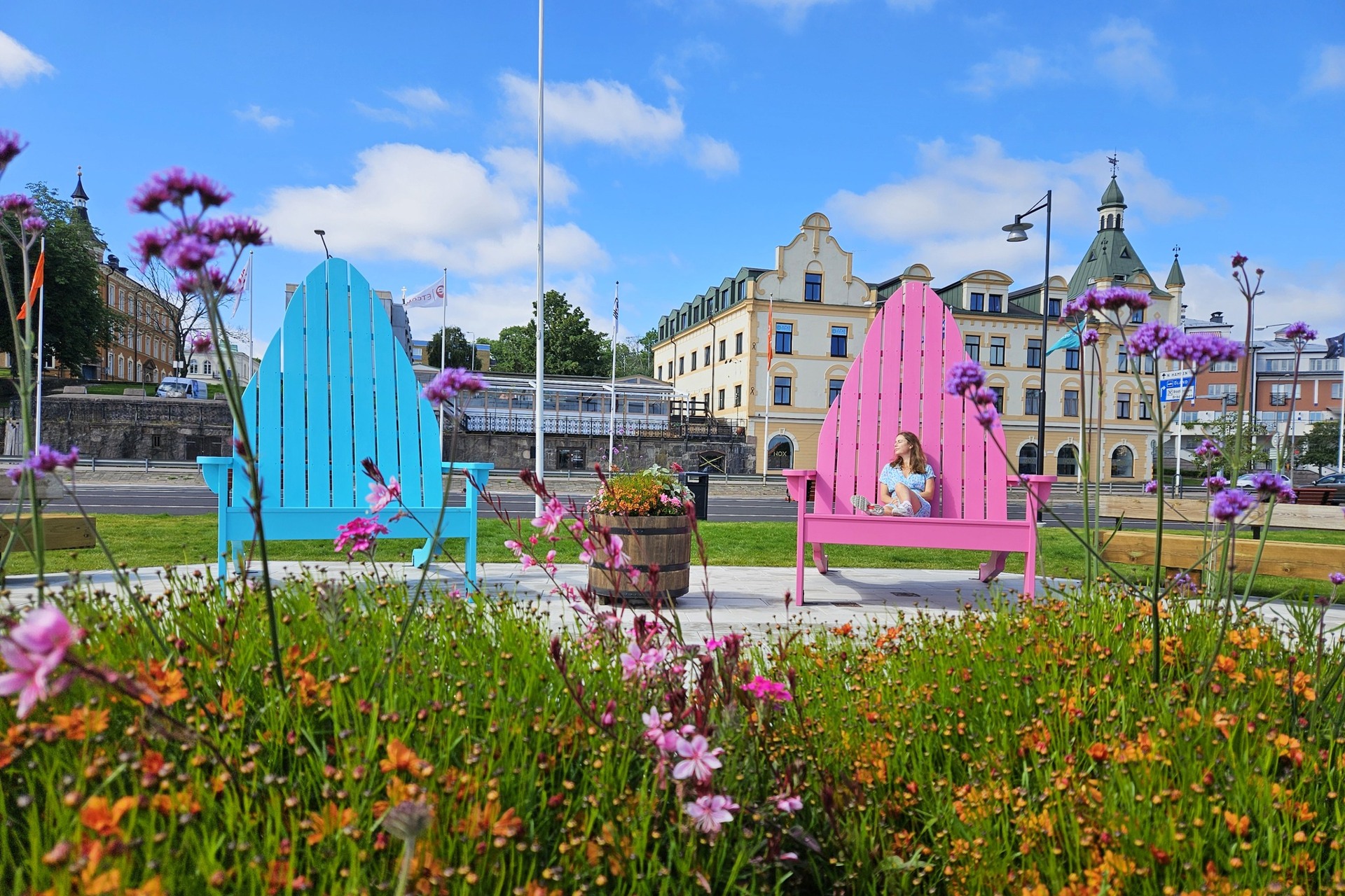 Person som sitter på en utav två färgglada jättestolar vid hamnen i Oskarshamn.