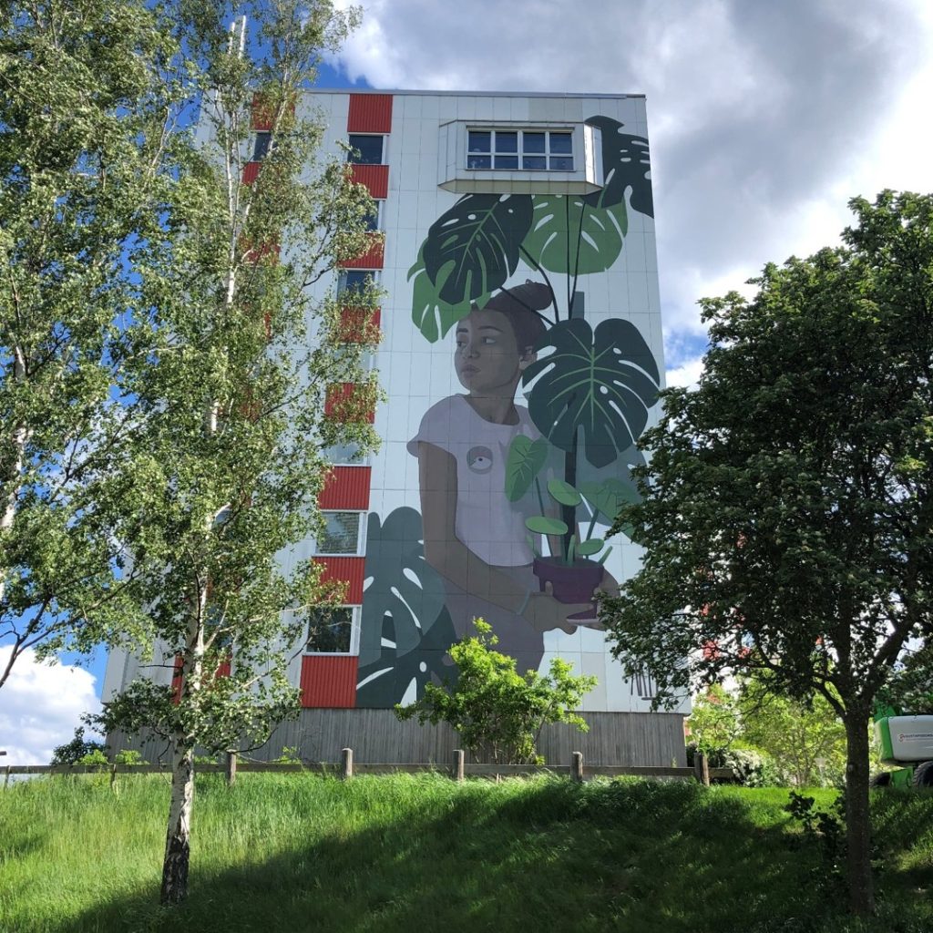 Väggmålning på höghus i Kristineberg i Oskarshamn, föreställande en ung flicka och en storbladig grön växt.