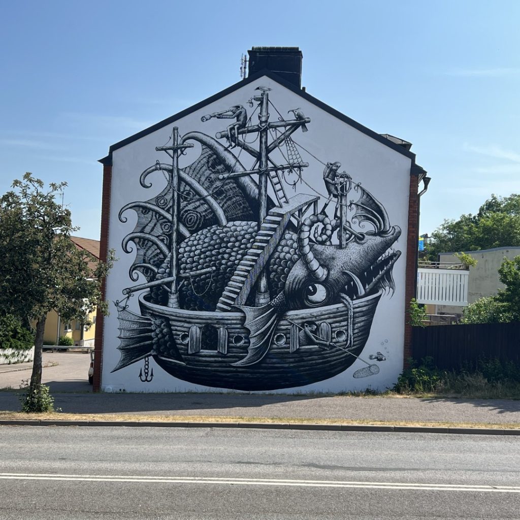 Svartvit väggmålning i centrala Oskarshamn föreställande ett sjöodjur i ett träfartyg.