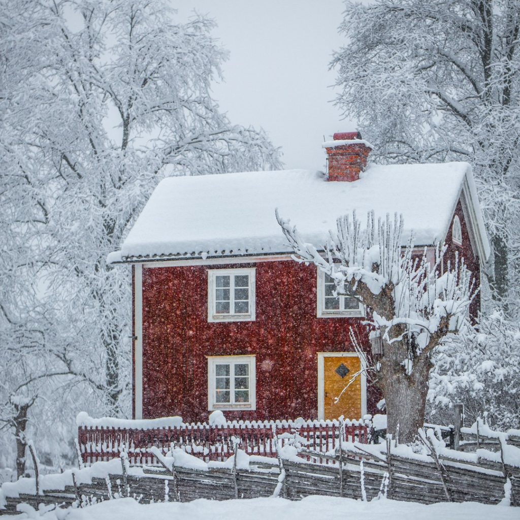 Bild på röd stuga med vita knutar i snöskrud i Stensjö by. Fotograf Frida Persson.