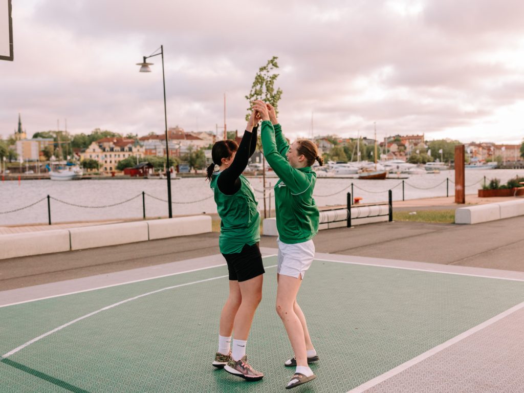Två personer gör high five på en basketplan, med glada miner och rörelse i bilden.