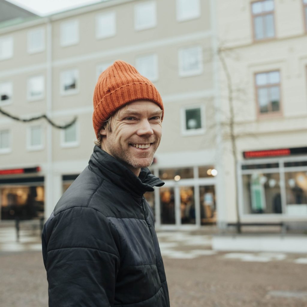 Erik Hjertqvist tittar leende mot kameran utanför Dressman i Oskarshamn, iklädd en orange mössa.
