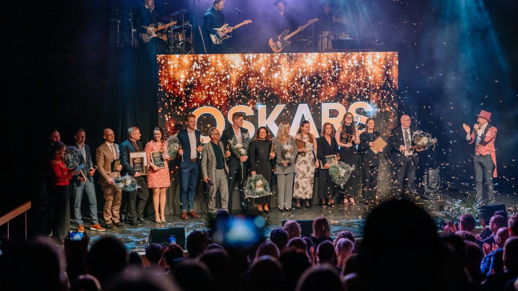 Ett regn av guldfärgad konfetti faller över pristagare på scenen på Oskarsgalan i Oskarshamn, ovanför vilket ett band står för att underhålla.
