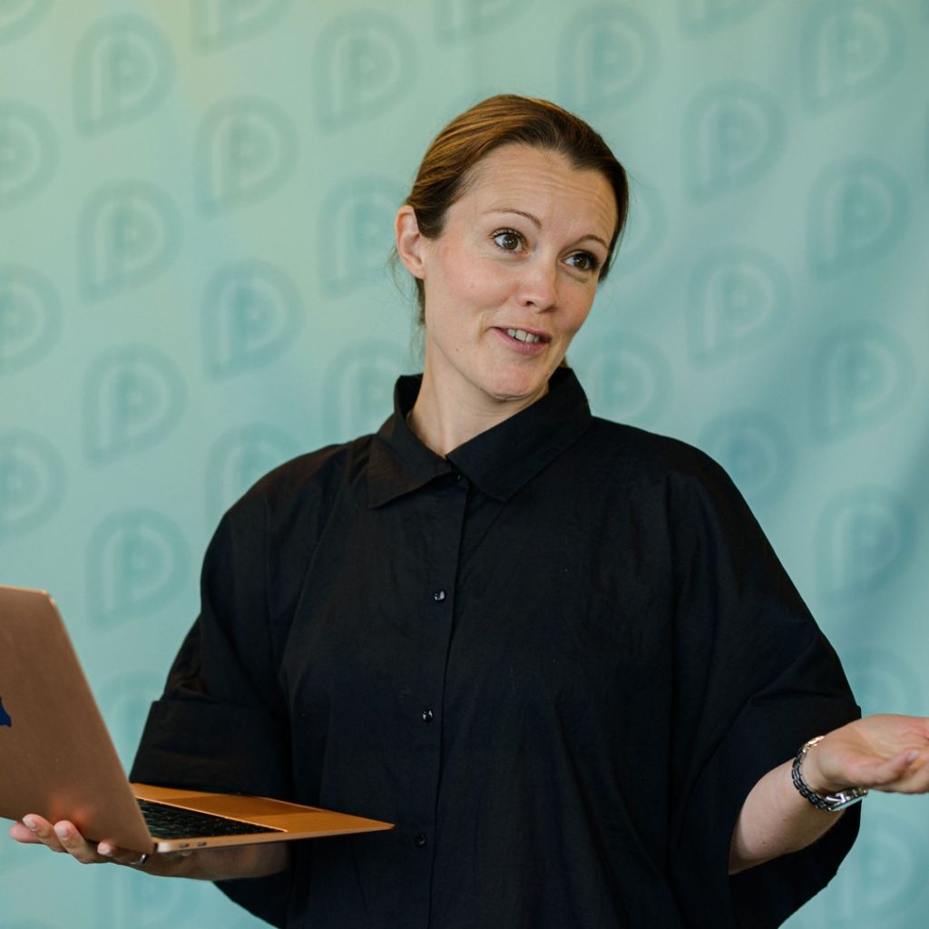 Sofie Gunnarsson håller ett anförande med en laptop i ena handen.
