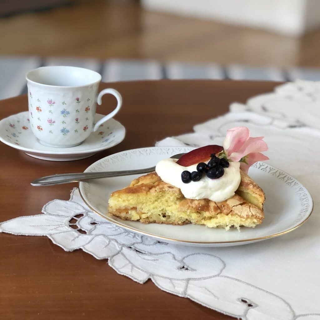 Vitt fat med dessert och kaffekopp på träbord med vit duk.