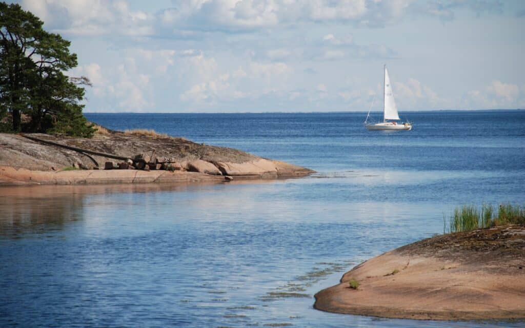 Stilla hav med öar och en segelbåt som glider fram under en blå himmel med vita moln.